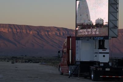 A large screen is mounted on a truck for spectators to view the Goddard launch. The Texas mountains are visible in the background at sunrise.