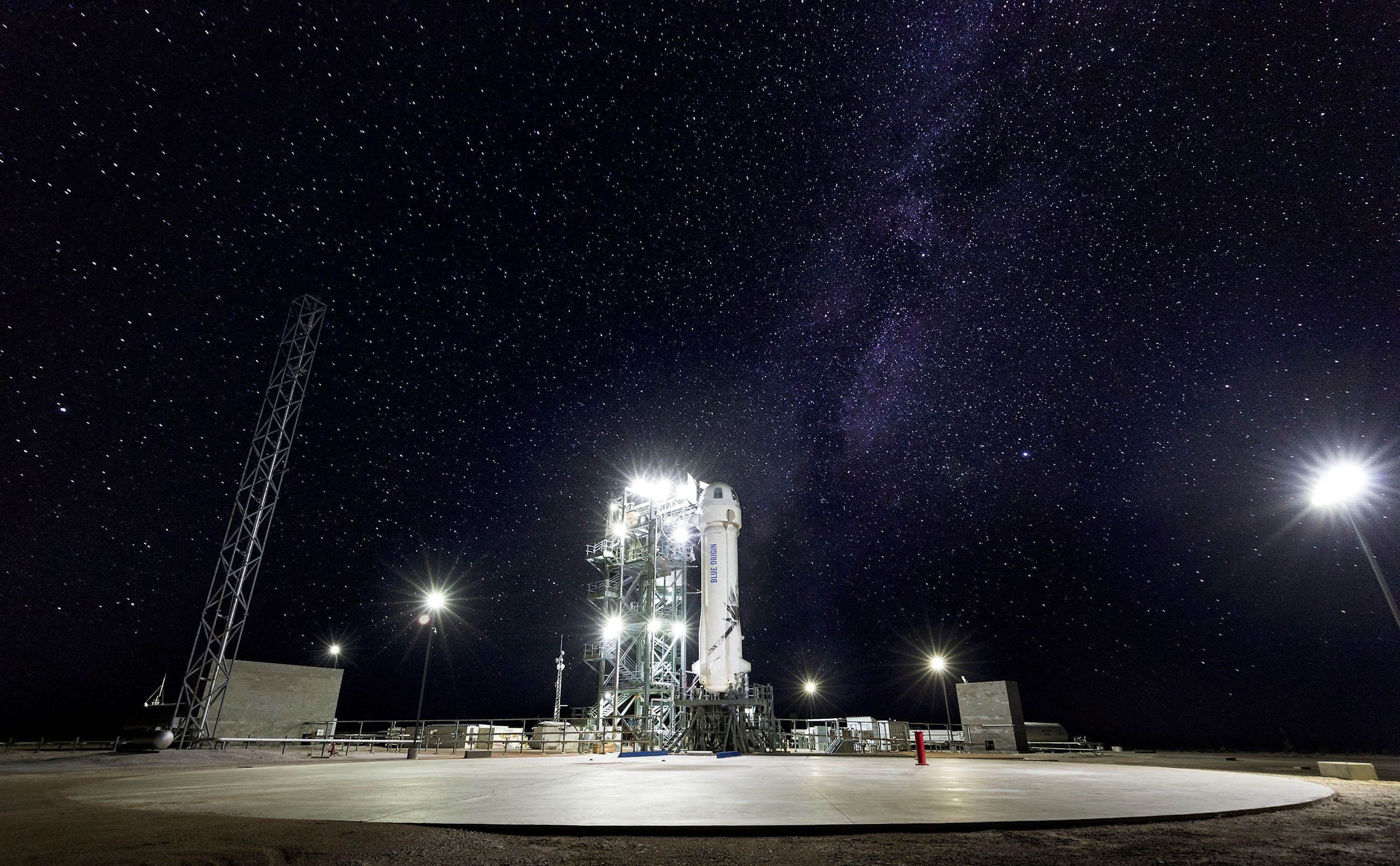 New Shepard is perched on the launch tower at night. The structure is brightly lit against a black starry sky.