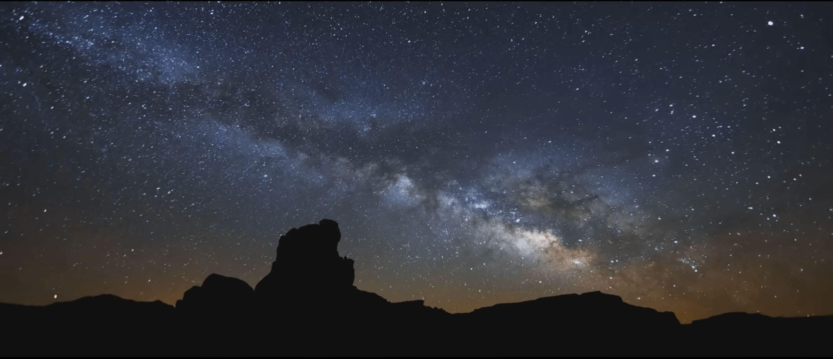 A starry night sky above shadowed desert rock formations.