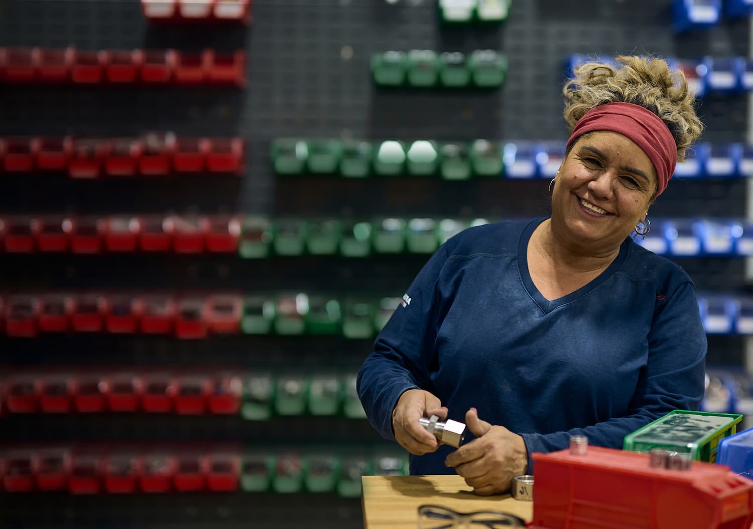 A woman working with small rocket parts at a workstation in front of a wall of part bins