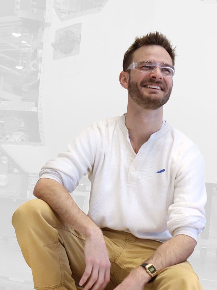 A young man with safety glasses and a Blue Origin shirt sitting superimposed on top of an assembly room