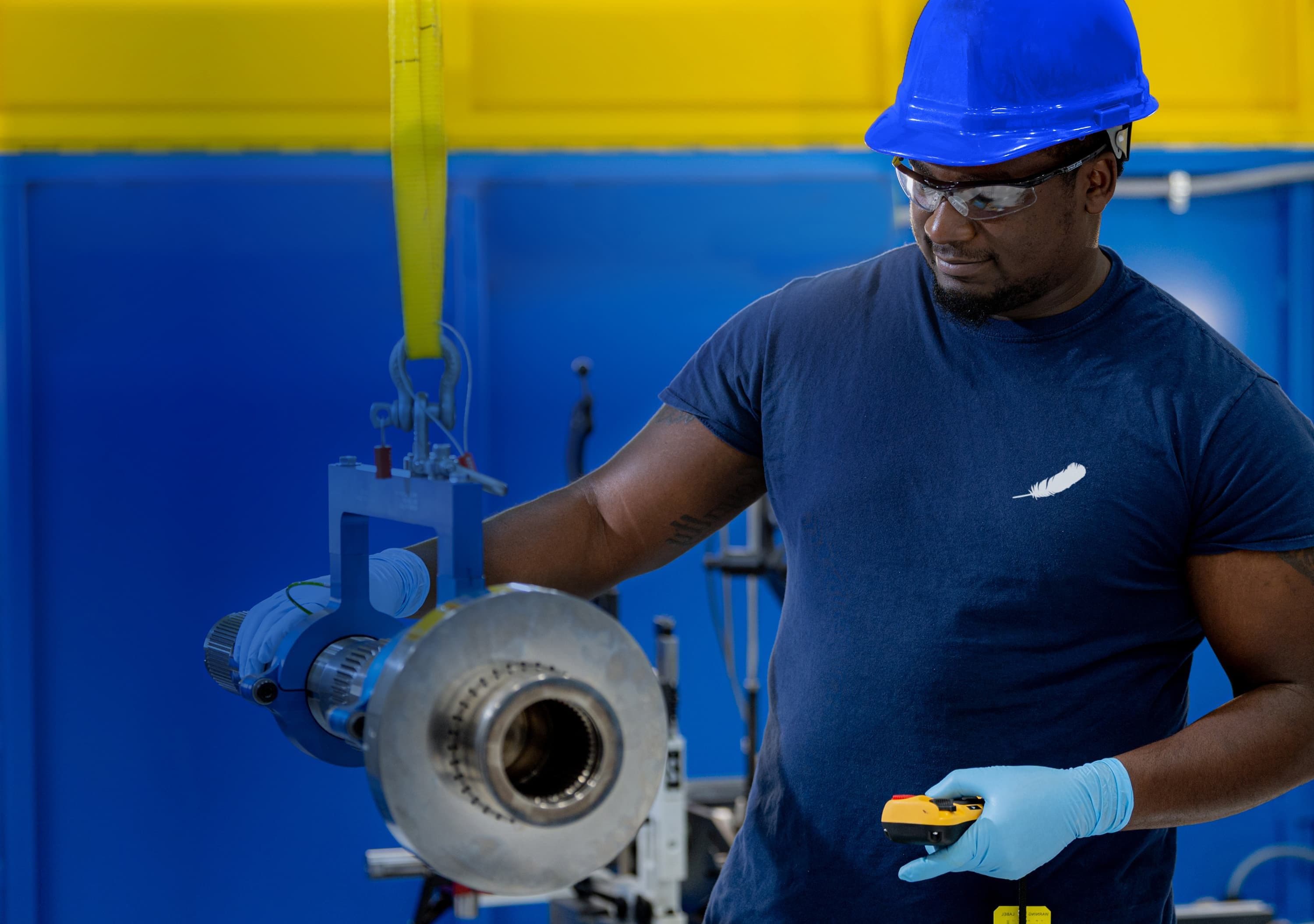 A man in a hard hat operating a handheld tool on a hoisted rocket part