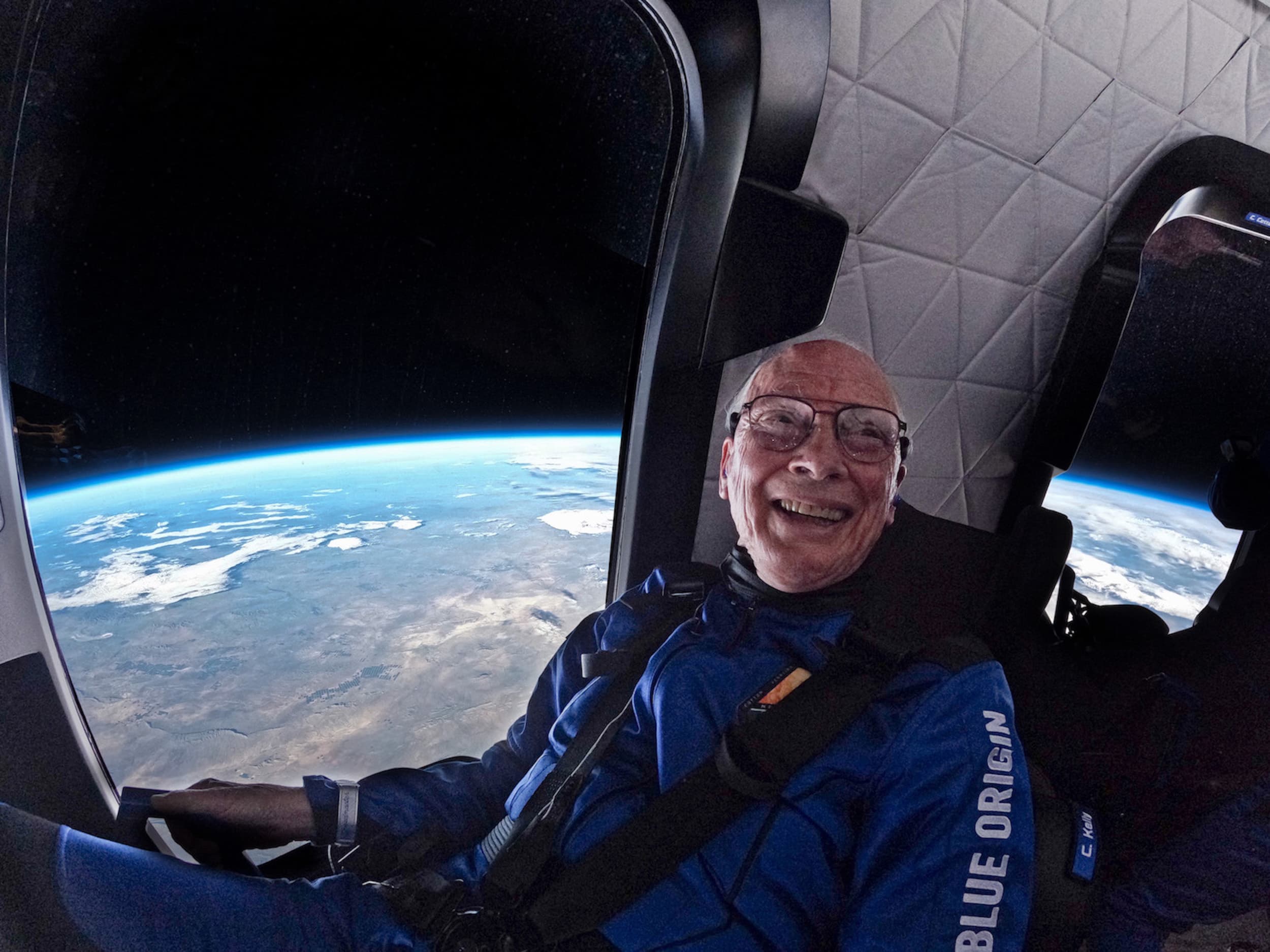 Clint is harnessed to his seat inside the crew capsule looking jubilant as Earth and the thin blue line of its atmosphere is visible through the window next to him.