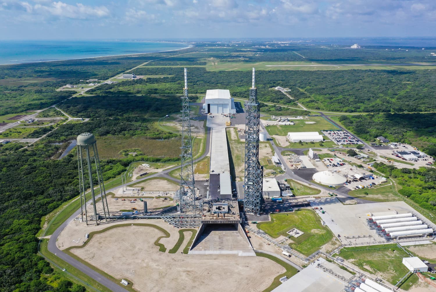 An aerial view of Launch Complex 36, located on the coast of Cape Canaveral, where New Glenn will launch. Two lightning towers, a large white building, and a water tower are in view.