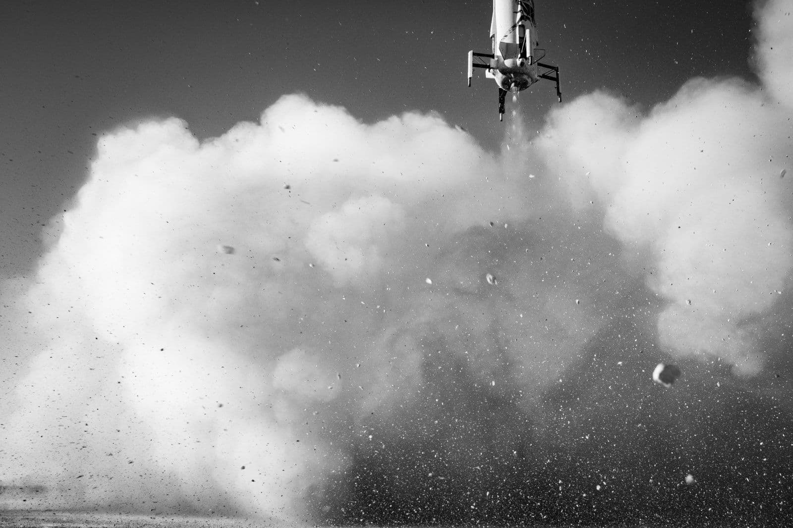 A black-and-white photo of the bottom of the booster, including the landing legs. Thick clouds of dust, smoke, and small rocks fill the frame.