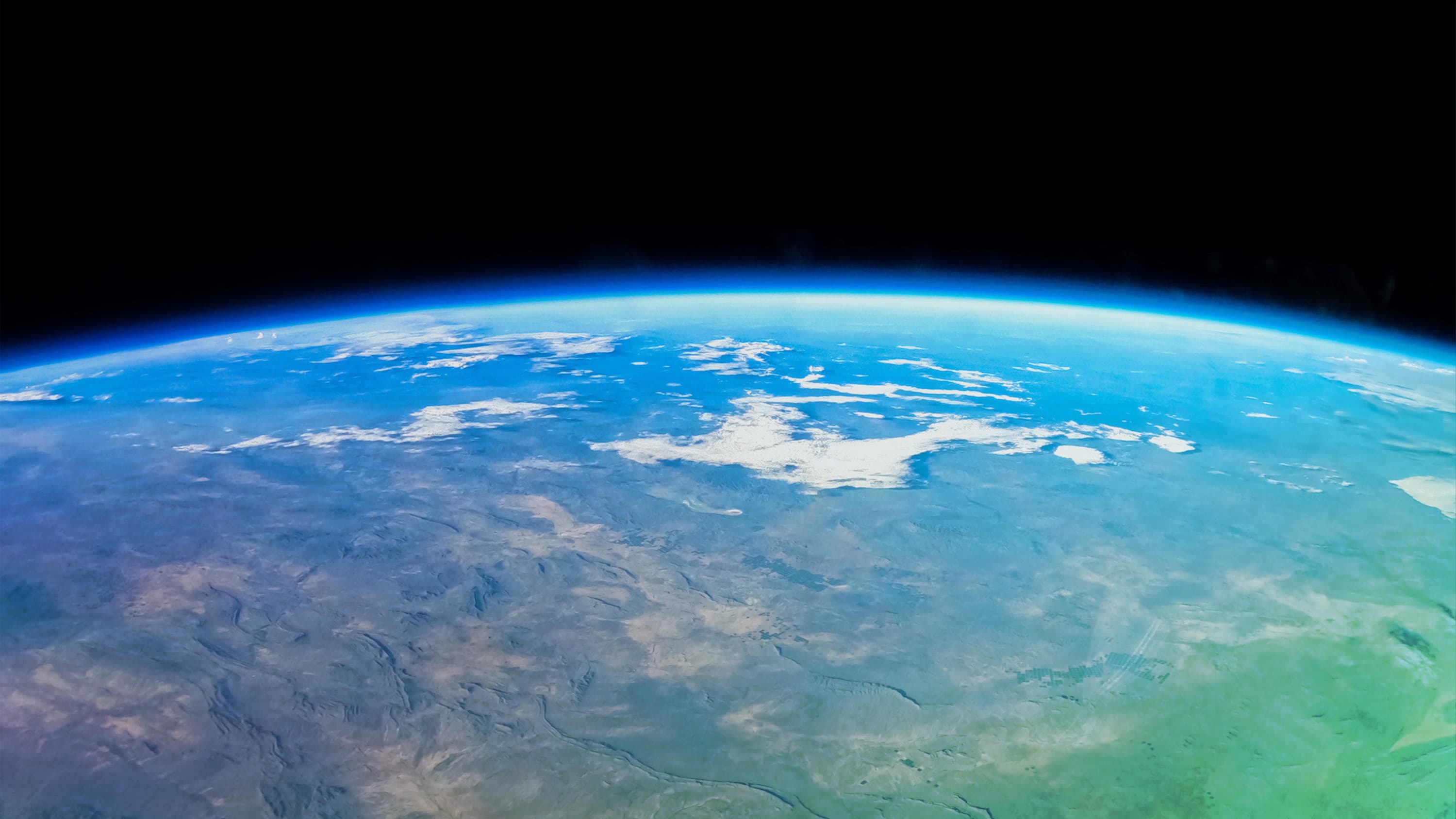 Earth and the thin blue line of its atmosphere, with a faint green overlay, as seen from inside the New Shepard crew capsule.