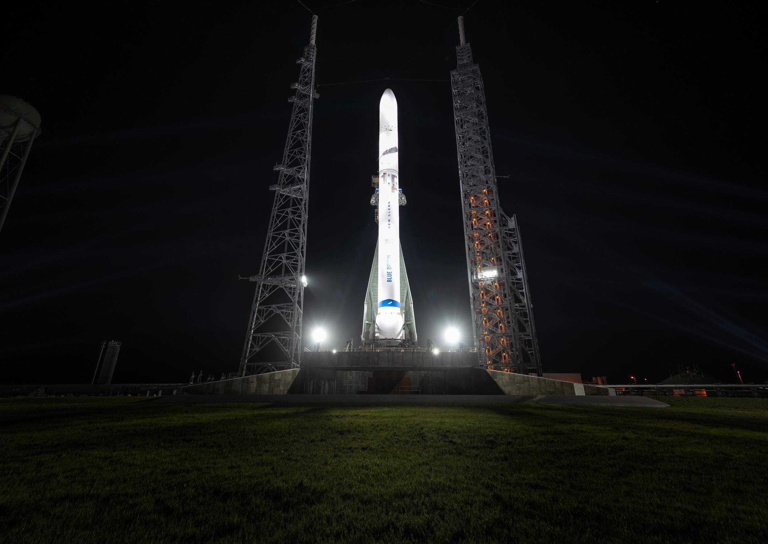 A white rocket lit by spotlights stands upright against a dark sky.