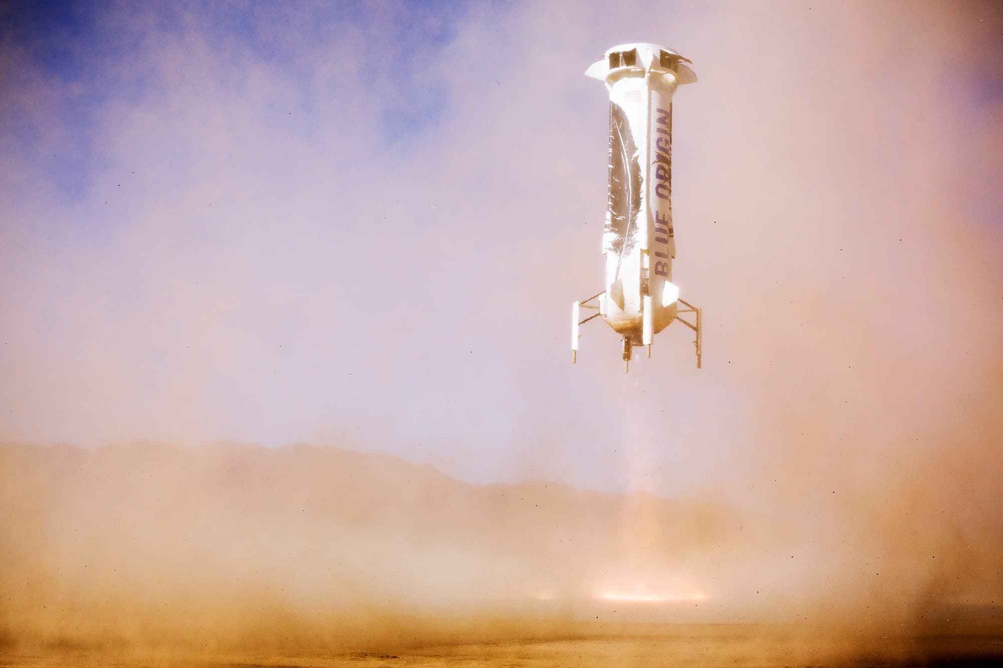 New Shepard’s booster hovers over the pad as the engine reignites and scorches the pad before landing.