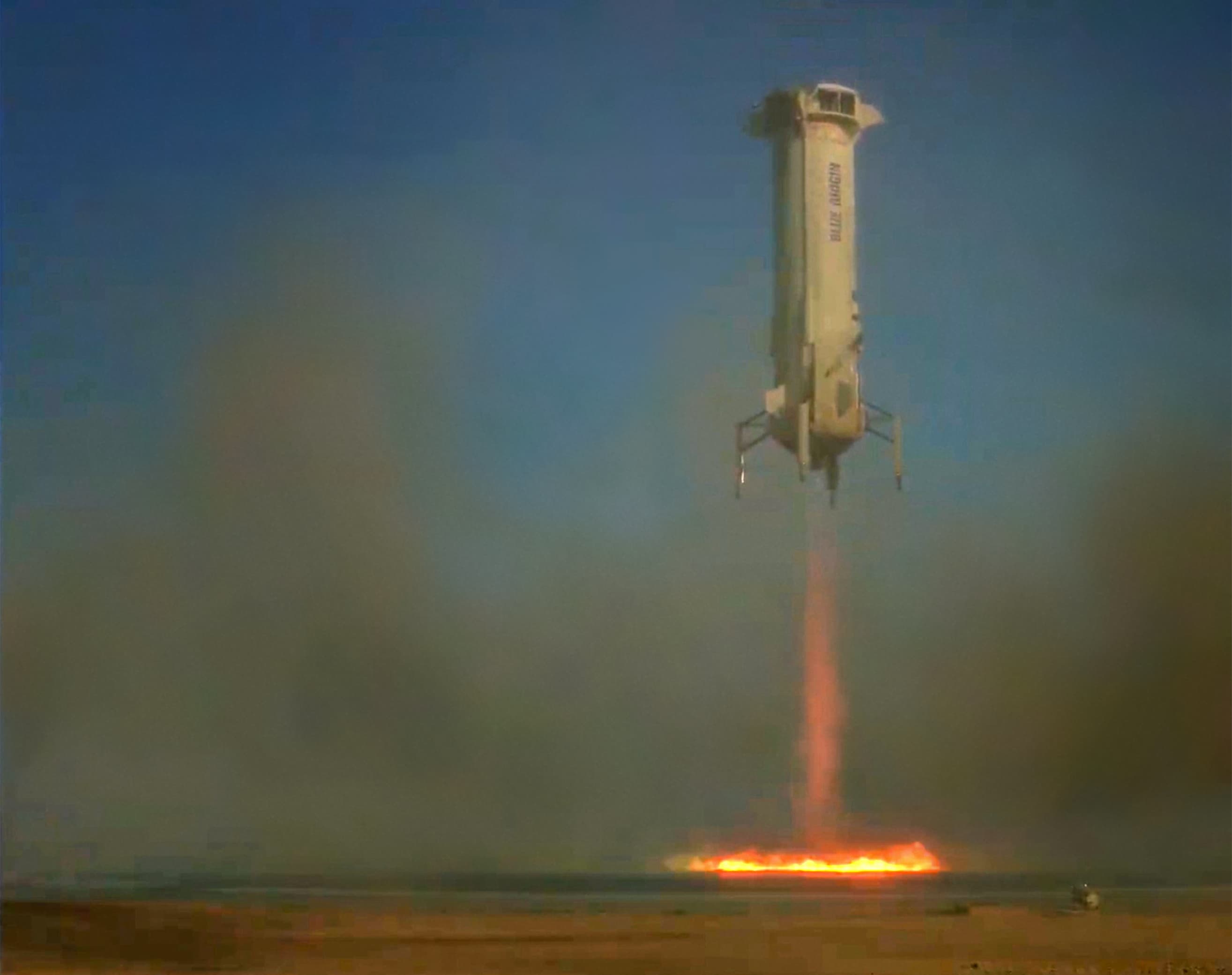 The booster expels smoke and orange exhaust, kicking up dust as it descends. The bottom half of the frame is dark and smoky.