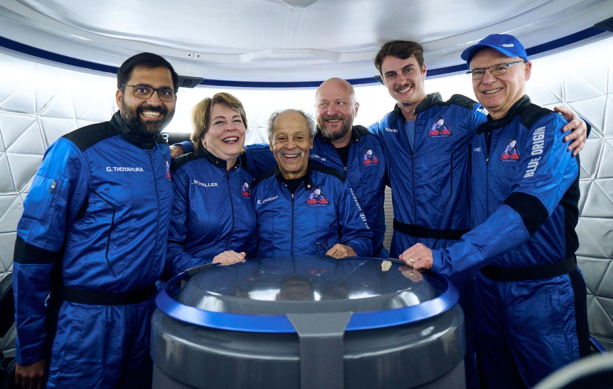 The NS-25 crew stands in the crew capsule in their blue flight suits.